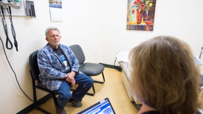 Doctor takes notes on tablet while spaking to patient in a clinic exam room.