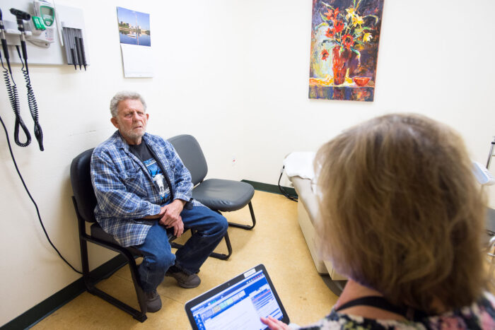 Doctor takes notes on tablet while spaking to patient in a clinic exam room.