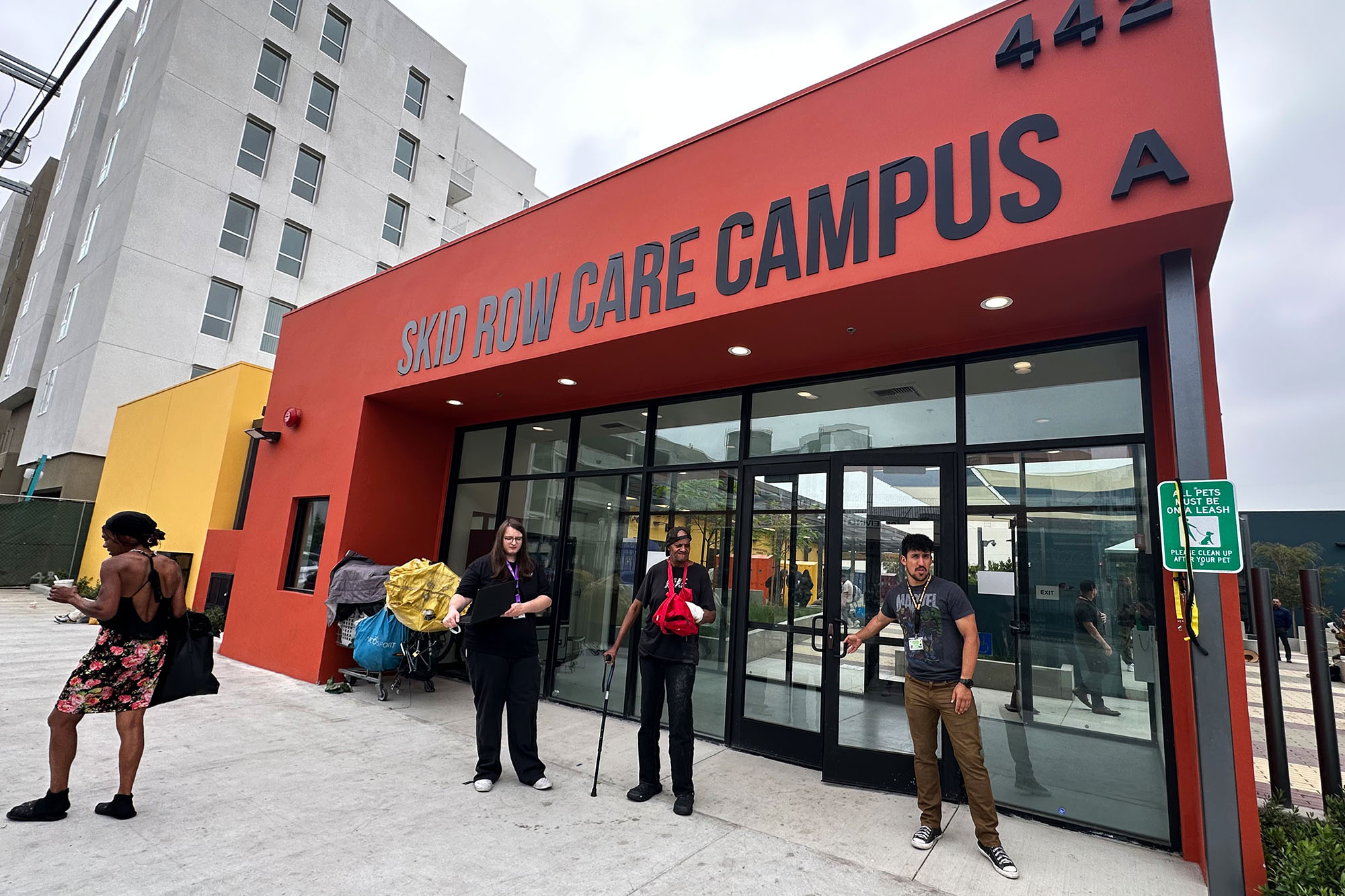 Four people standing in front of the Skid Row Care Campus in Los Angeles, a plave where people expriencing homelessness can get health care , find a place to rest, charge their phones, grab some food, or even get connected with housing.