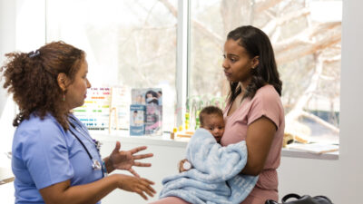 A healthcare professional consults a mother holding her baby in a medical clinic setting.