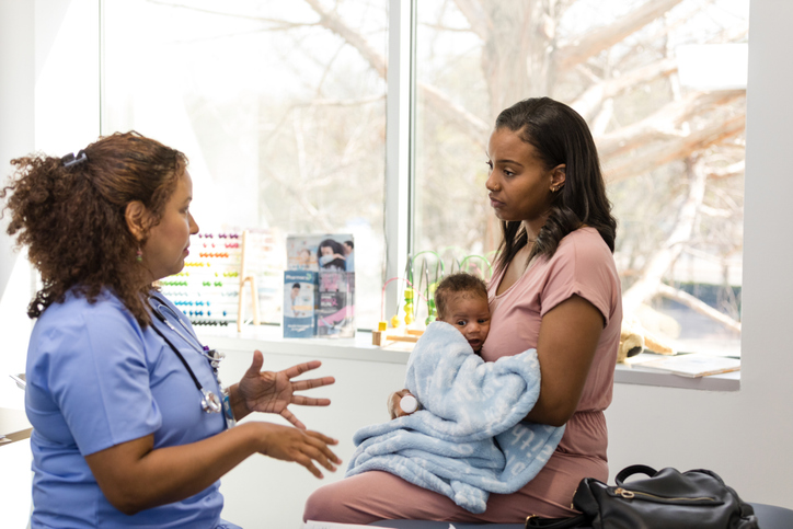A healthcare professional consults a mother holding her baby in a medical clinic setting.