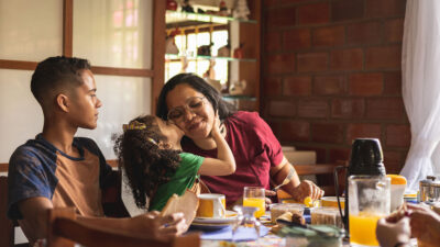 Mother daughter and son at breakfast table. Daughter is giving her mother a kiss on the cheek.