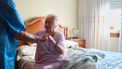 Home health care worker helping client rise from bed.