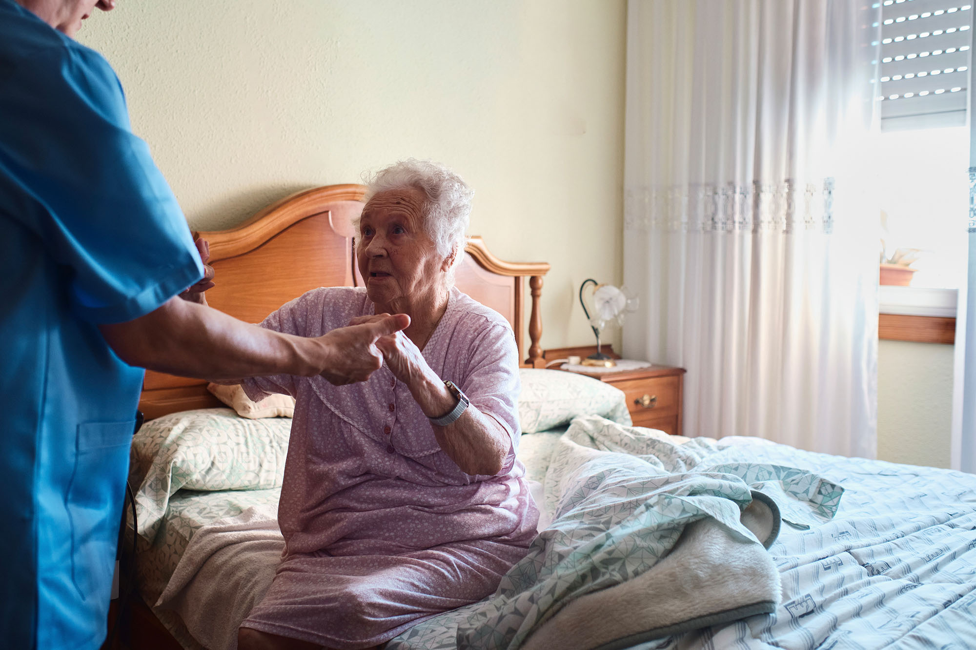 Home health care worker helping client rise from bed.