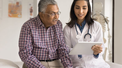 Elderly man looks at tablet with doctor