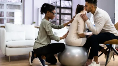 Two people provide care to an expectant mother on an exercise ball