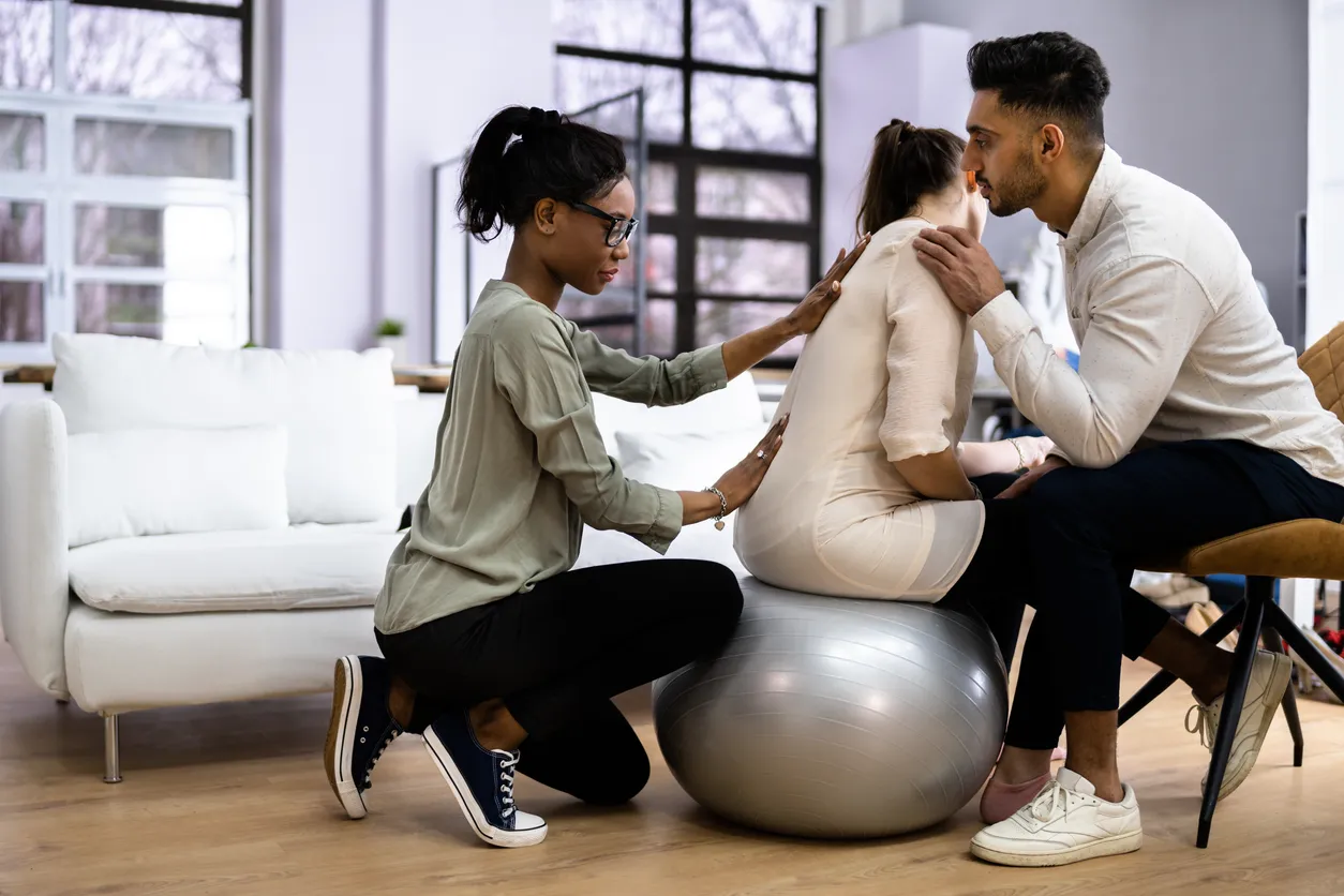 Two people provide care to an expectant mother on an exercise ball