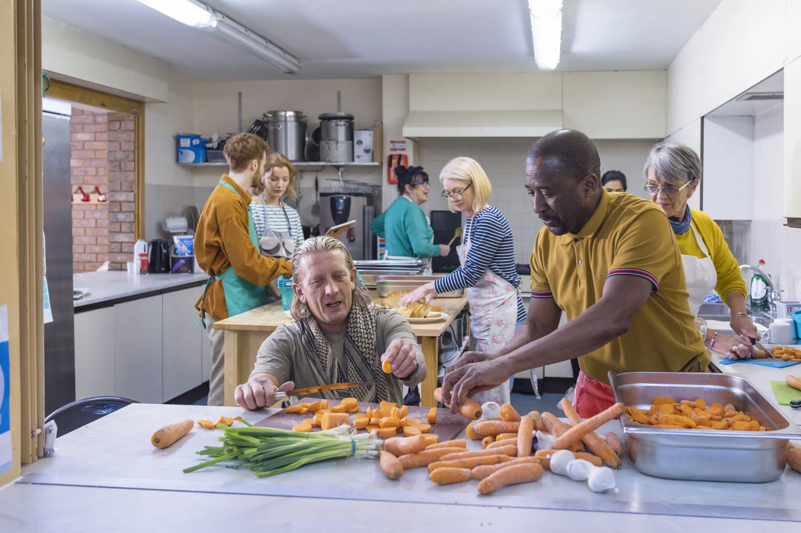 Group of men and women prepare food together in a community kitchen